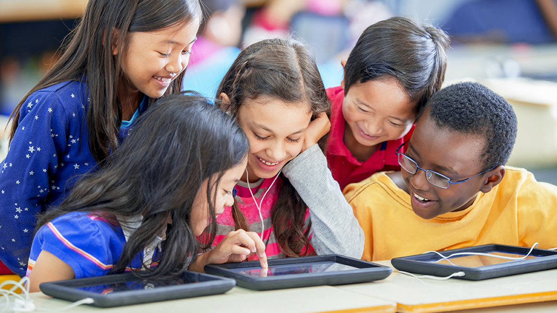 Children playing and observing a digital game on a device or tablet.