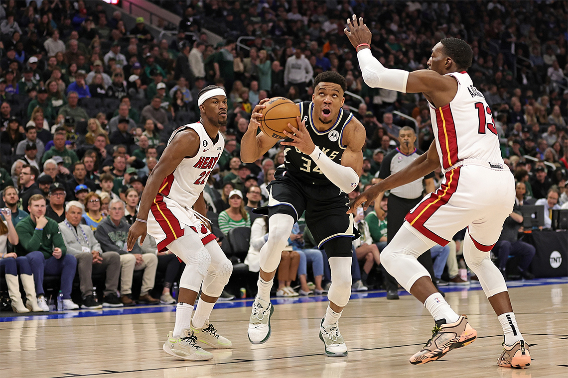 Giannis Antetokounmpo #3 of the Milwaukee Bucks (2023) running while holding the ball, while two other Miami Heat players look on.