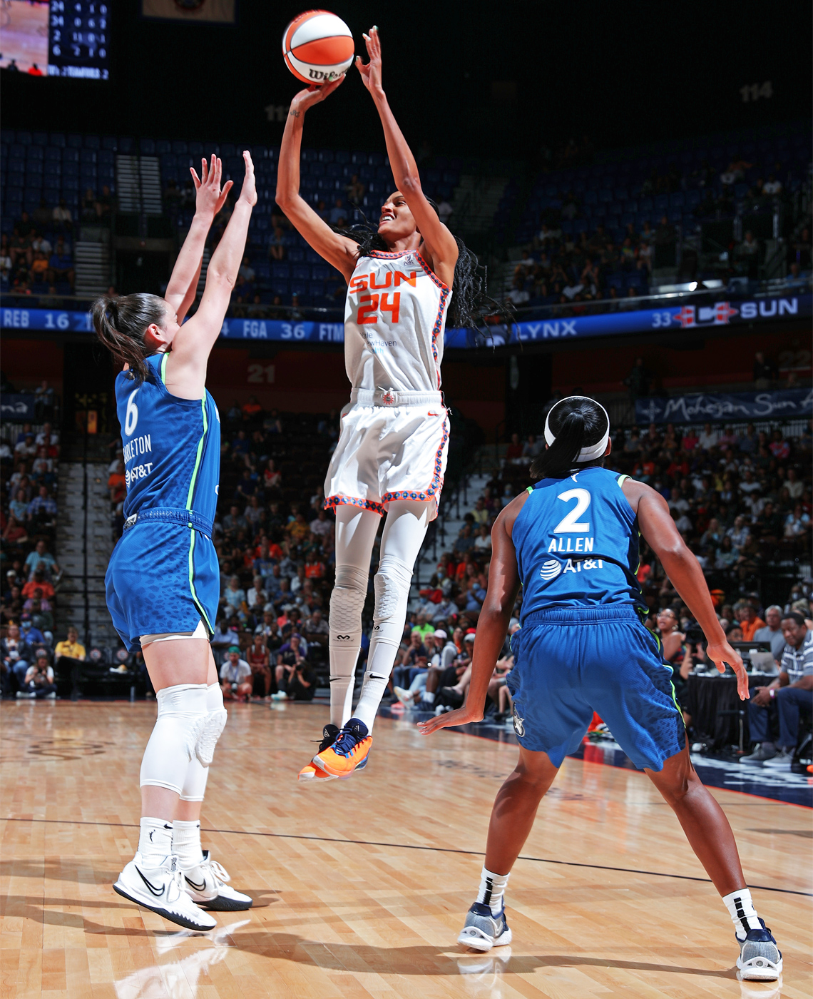 DeWanna Bonner jumping while throwing the basketball into the basket. One opposing player reaches up to defend, and another is crouched.