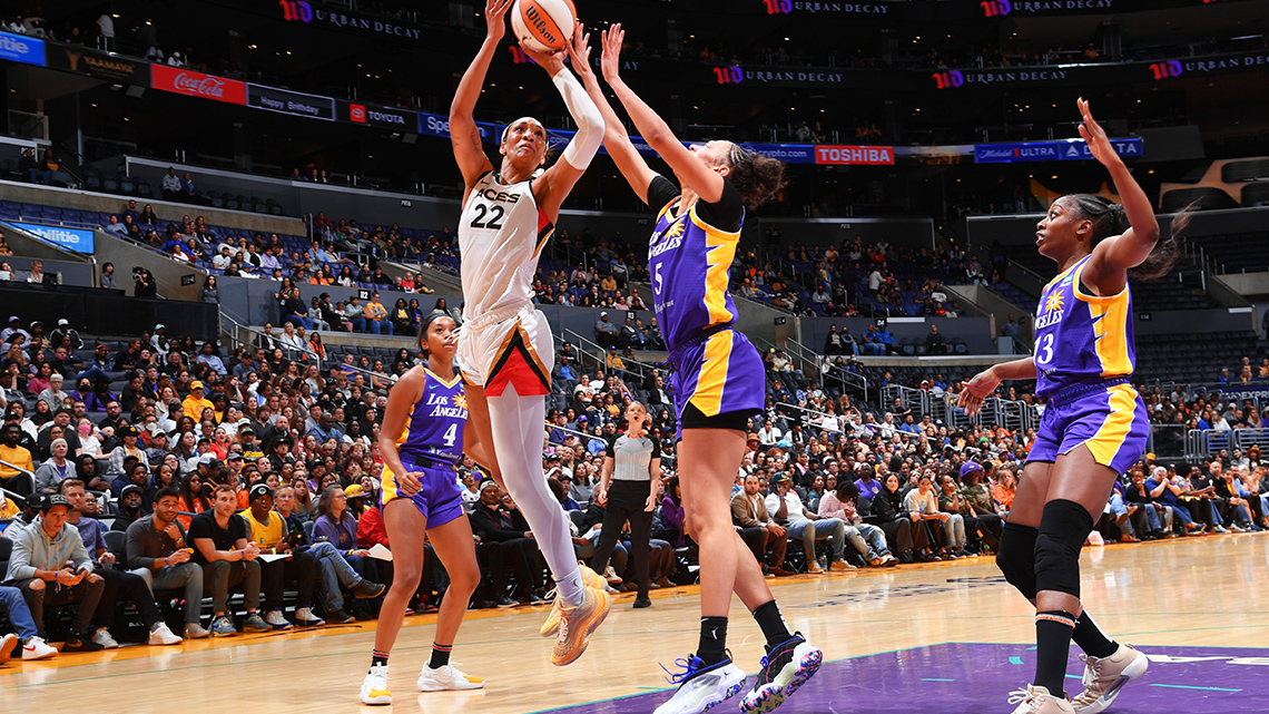 A’ja Wilson, #22 of the Las Vegas Aces, jumps and throws the ball, when an opposing player defends the ball. Other opposing players look on.