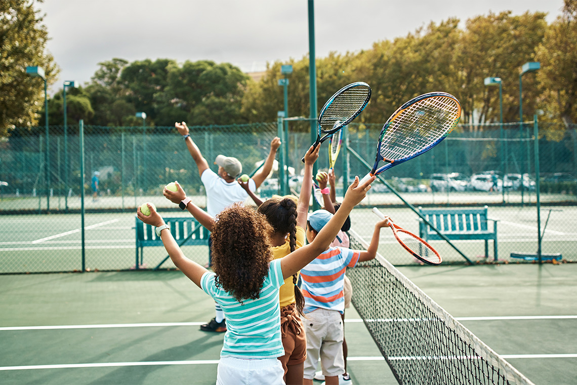 Children learning to play tennis while holding tennis rackets and tennis balls on a tennis court.