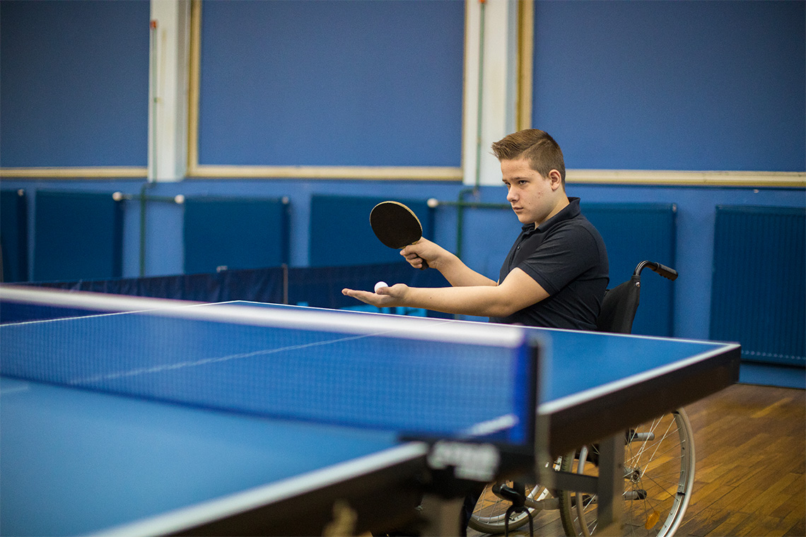 Person playing indoor table tennis, with hand outstretched with the ball, and other hand with the paddle.