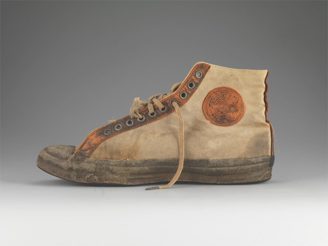 Original converse All star Chuck Taylor Basketball shoe with laces from the front bottom up, and with rubber soles. Natural brown shoe with black trim.
