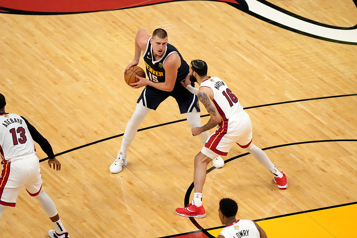 Nikola Jokić, #15 of the Denver Nuggets (2023), handles the basketball against two opposing defense players.
