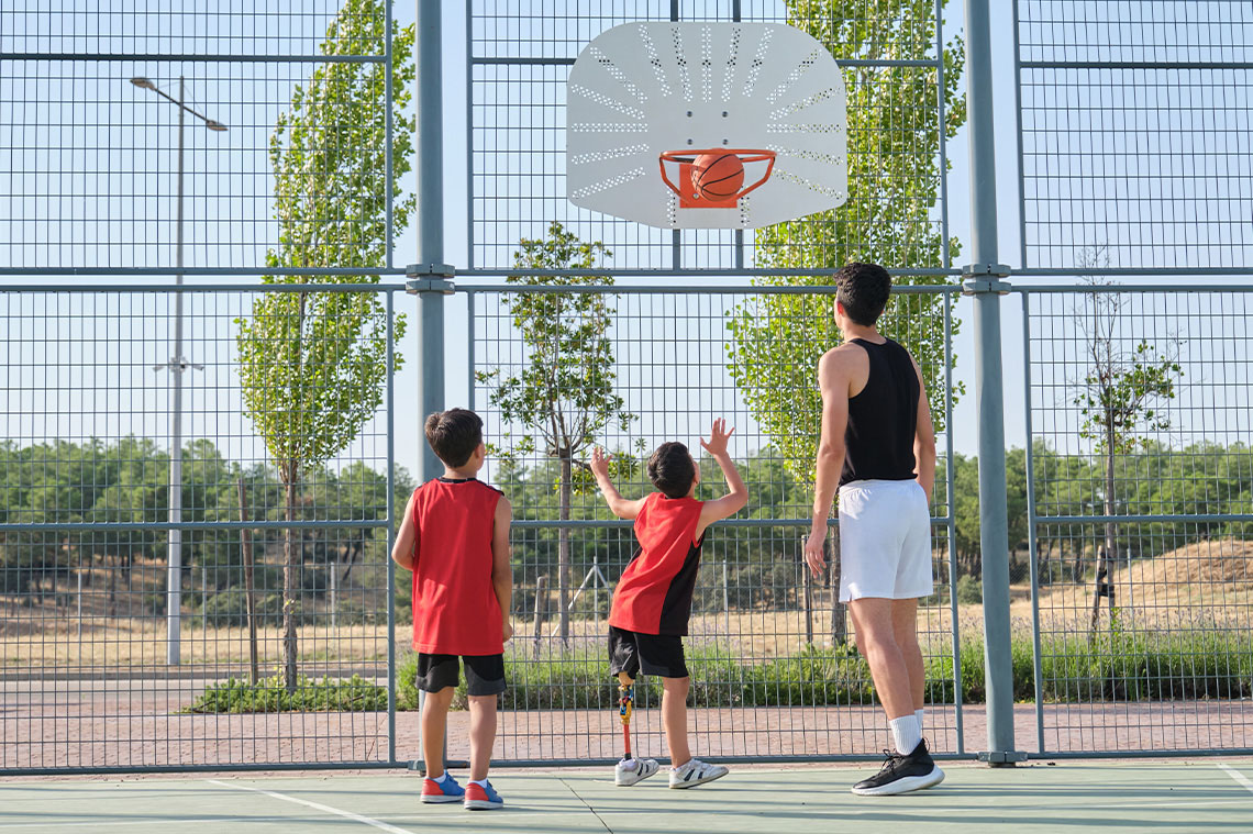 Child shooting a basketball in the net while two other individuals look on.