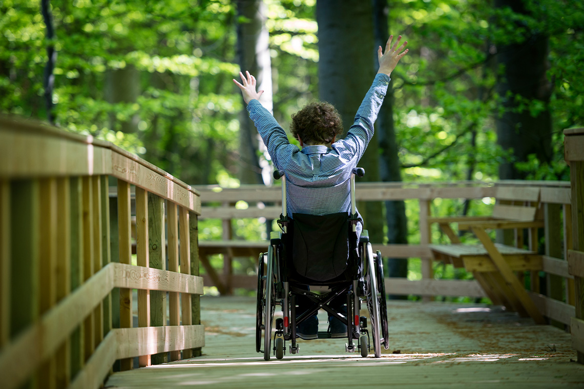 Student seated in a wheelchair with their hands raised.