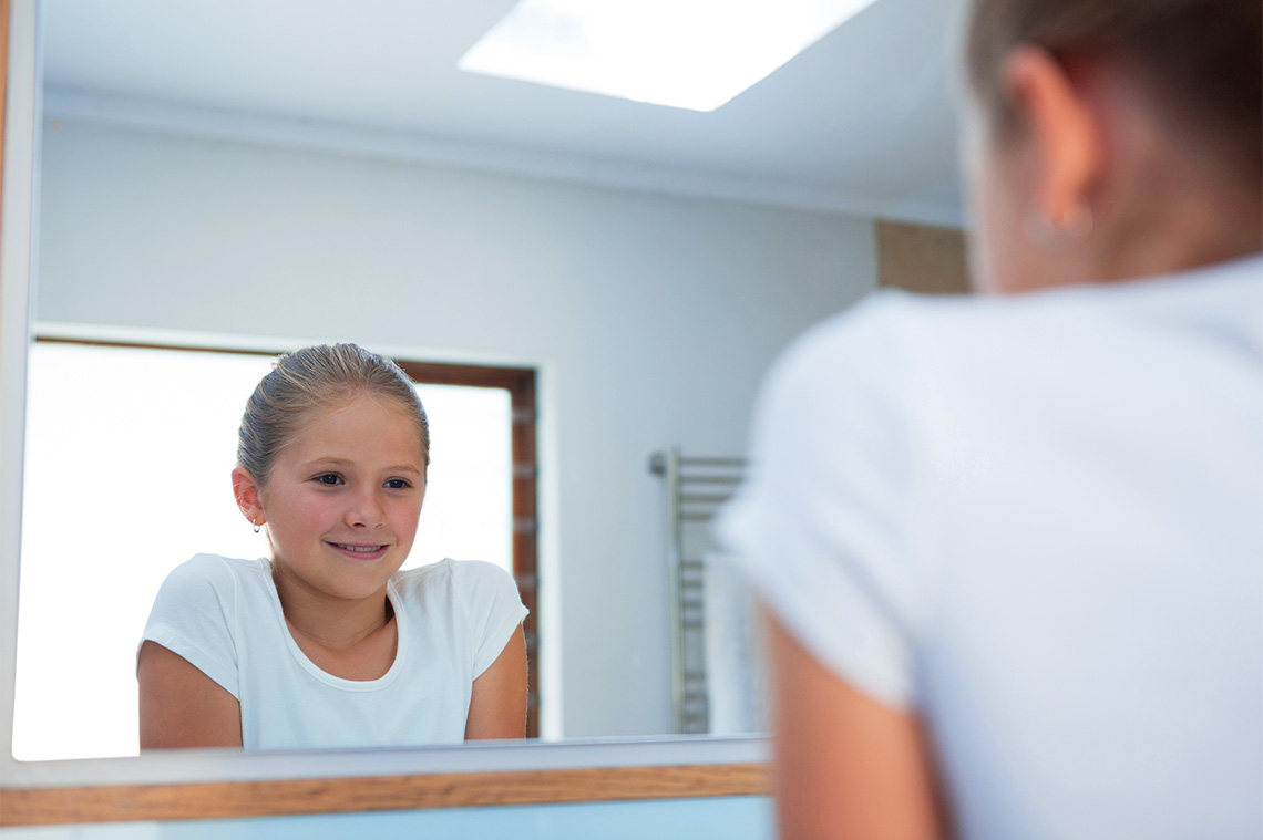 Teenager smiling while looking at themselves in the mirror.