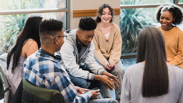Group of teens seated together as a peer shares their experiences. Peers supporting each other.