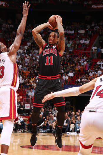 Demar DeRozen, #11 of the Chicago Bulls (2023), jumps to dunk the basketball into the net; opposing players outstretch their arms to defend.