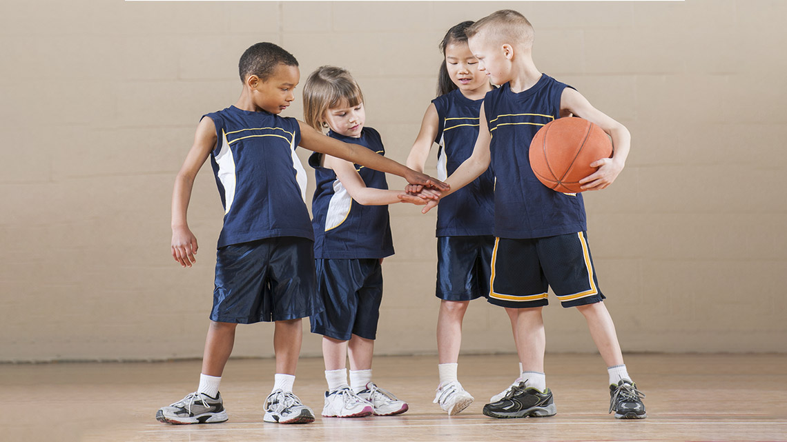 Young basketball players stand in a circle. They all put a hand in so that all of their hands are connected.