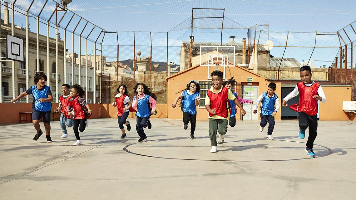 A group of children run together across an outdoor basketball court.