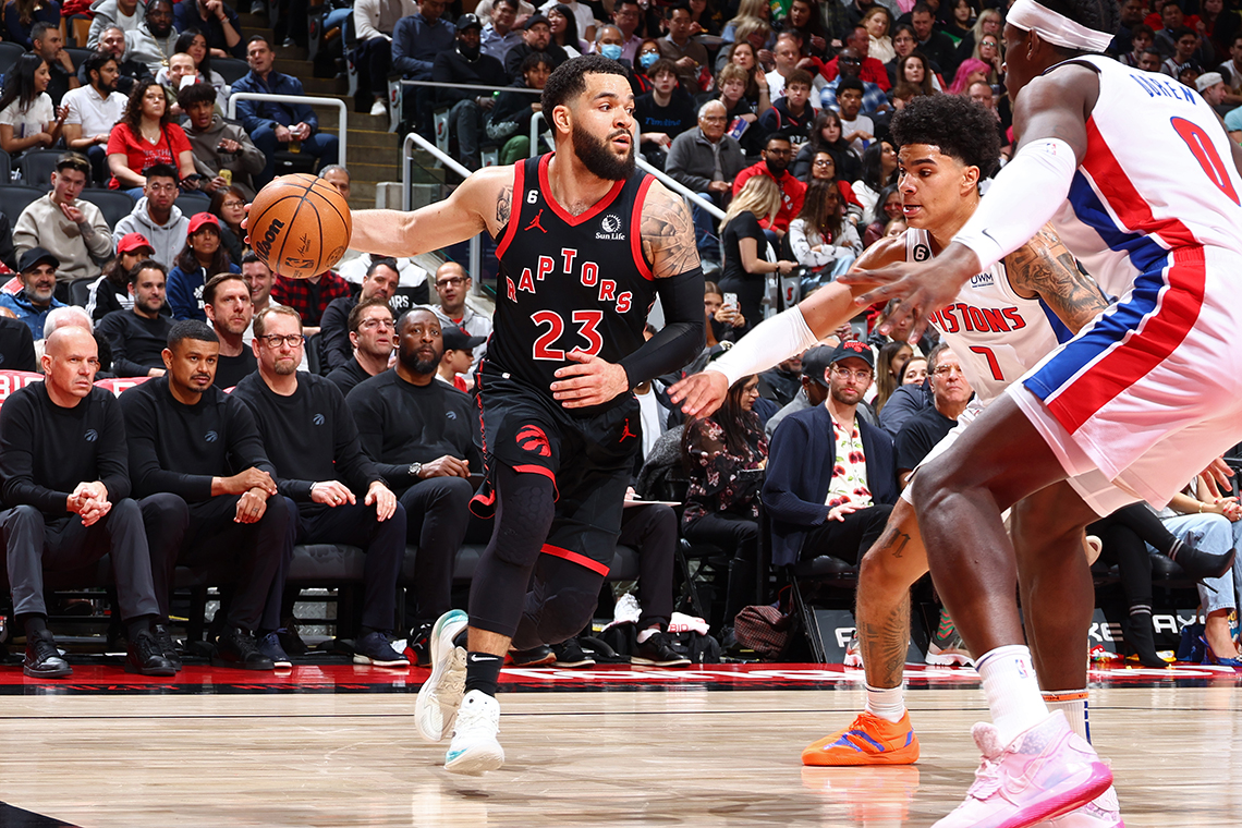 Fred VanVleet bounces a basketball across a basketball court. Two other players stretch their arms out to defend against VanVleet.