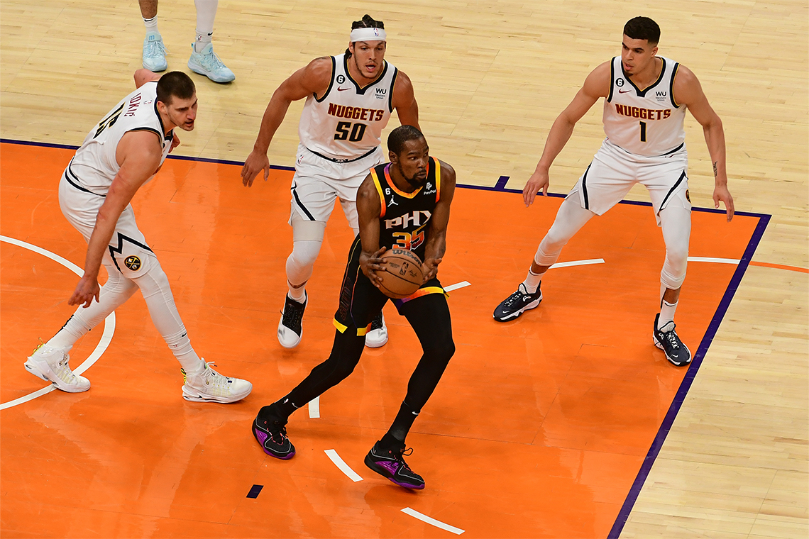 Kevin Durant bouncing the basketball while being flanked by 3 Denver Nuggets’ players.