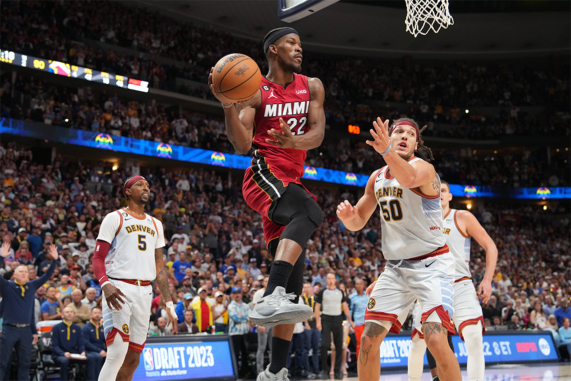 Jimmy Butler jumps mid-air while about to pass the basketball. Opposing players look on.