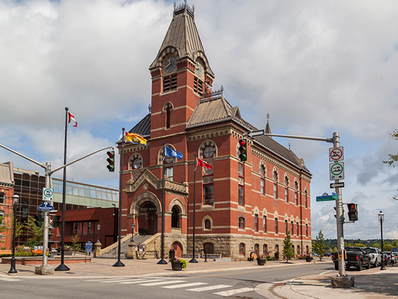 A historic building on a city street. It’s made of brick and stone, has arched windows, and a large clock tower above the main entrance