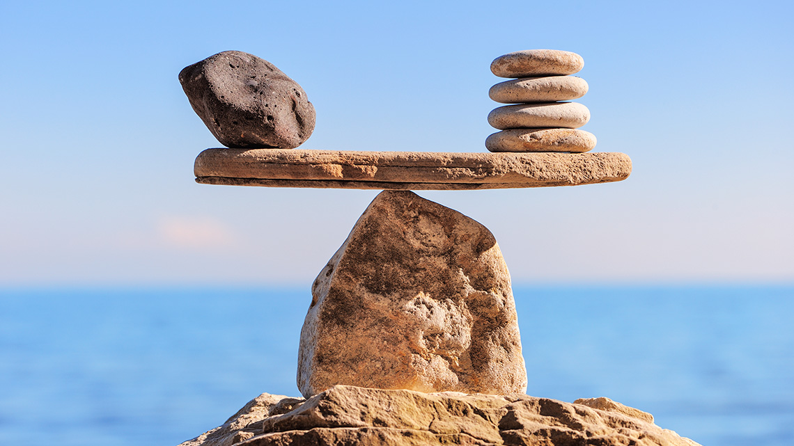 A scale is balanced with one large stone on the left side and four smaller stones on the right side